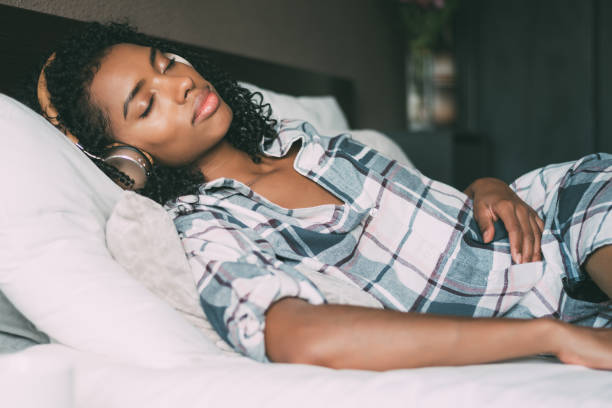 femme, dormir sur le lit et l’écoute de musique avec des écouteurs et smartphone - using computer bedroom one woman only cheerful photos et images de collection