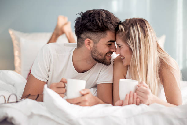 Sweet young couple lying in bedroom Young beautiful couple drinking coffee in bed at morning. boyfriend stock pictures, royalty-free photos & images