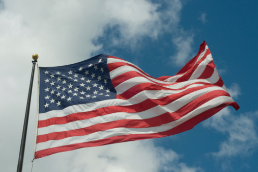 United States flag waving on a blue sky with white fluffy clouds