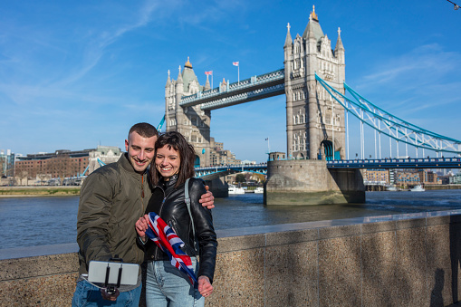 Shot of an affectionate young couple take selfie portrait with British flag at The Tower Bridge, London, England.