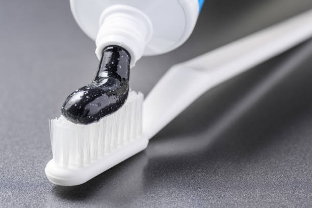 Black charcoal toothpaste being squeezed on white toothbrush stock photo
