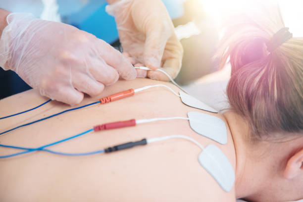istock Physical therapist positioning electrodes for high back muscle treatment 941018056