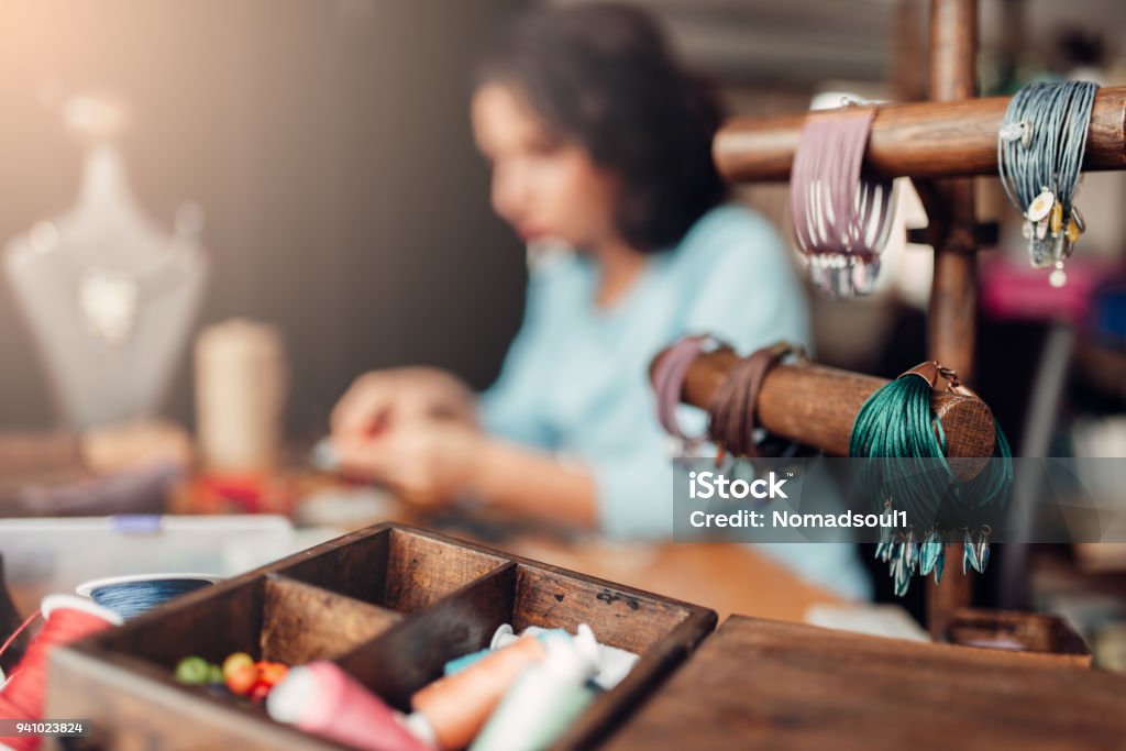 Needlework tools, master at workplace in workshop Needlework, box with accessories, bracelets, female master at workplace in workshop on background. Handicraft tools. Handmade fashion decor Jewelry Stock Photo