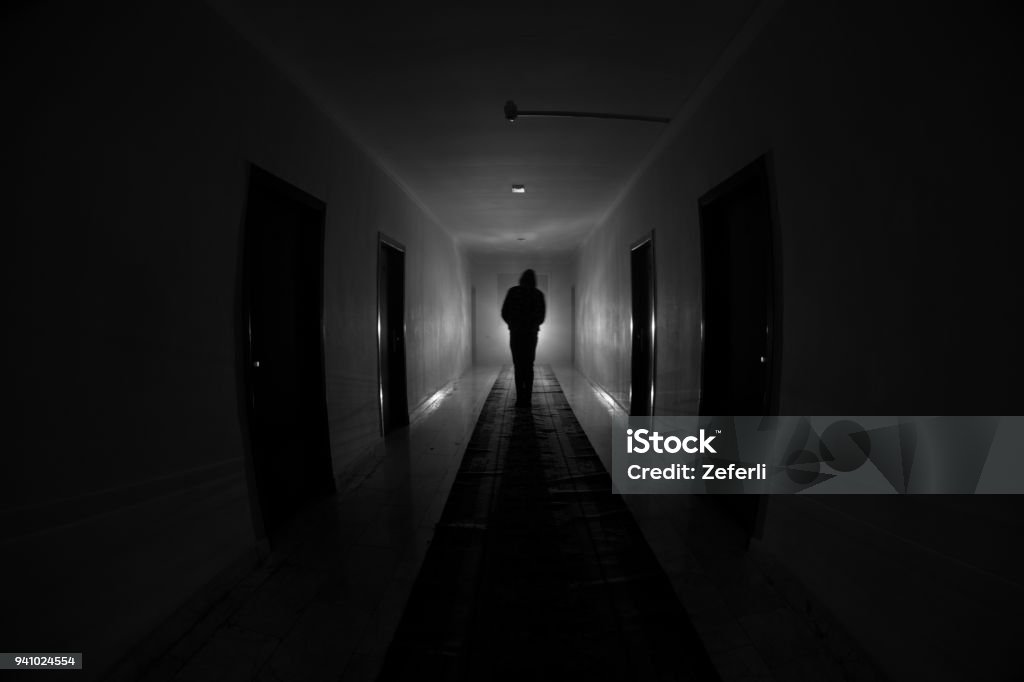 Creepy silhouette in the dark abandoned building. Dark corridor with cabinet doors and lights with silhouette of spooky horror person standing with different poses. Creepy silhouette in the dark abandoned building. Horror about maniac concept or Dark corridor with cabinet doors and lights with silhouette of spooky horror person standing with different poses. Spooky Stock Photo