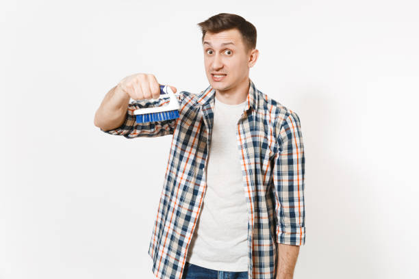 Young fun crazy dizzy loony wild housekeeper man in checkered shirt holding brush for cleaning isolated on white background. Male doing house chores. Copy space for advertisement. Cleanliness concept joven divertido a hombre de crazy dizzy loony salvaje del ama de casa en camisa a cuadros con cepillo para la limpieza aislado sobre fondo blanco. hombre haciendo las tareas de la casa. copiar el espacio para el anuncio. concepto de limpieza.