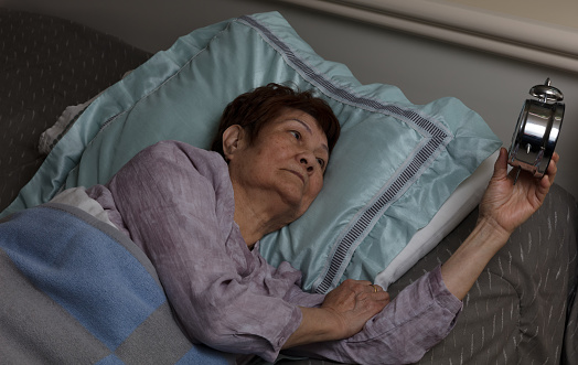 Restless senior woman glaring at her alarm clock during nighttime