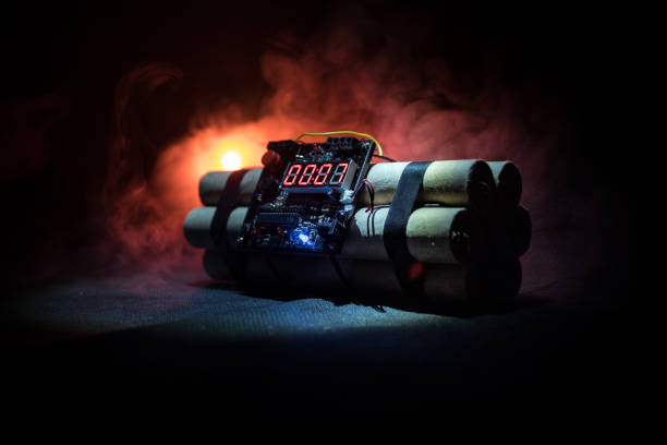 A human hand holding a ball bomb with a burning fuse on dark background