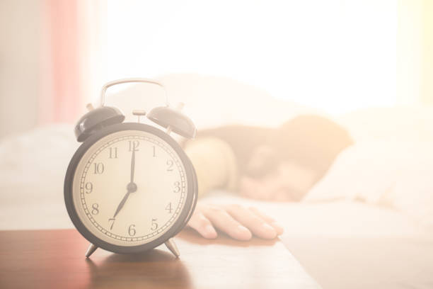 istock Alarm clock with a woman sleeping in the background on bed 941036318