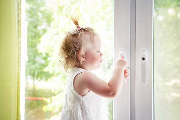istock small child is standing on windowsill and opens window. Locks on windows prevent children from falling out of window. Girl playing with window handle. 941036324
