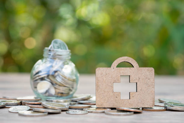 Wooden medical bag on coins stack with jar of coins as backdrop. Concept of money saving, financial, life insurance, retirement, investment. stock photo