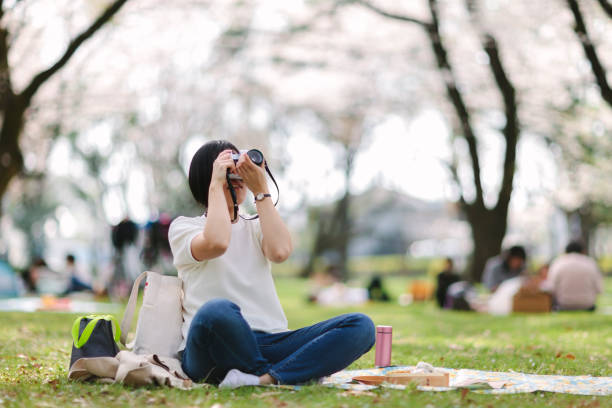 A young Japanese woman is taking photos with an old slr camera while having picnic.