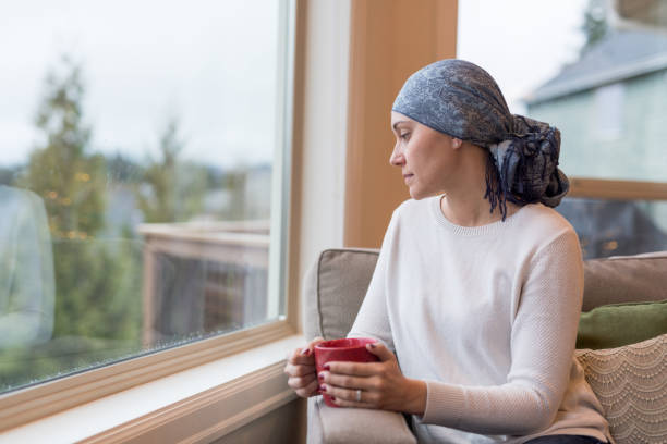 una sopravvissuta al cancro etnico di mezza età si siede vicino alla finestra e riflette sulla sua vita - cancer women womens issues friendship foto e immagini stock