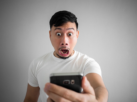 Shocked and scary face of Asian man get yelled from smartphone.  See something scary in smartphone.