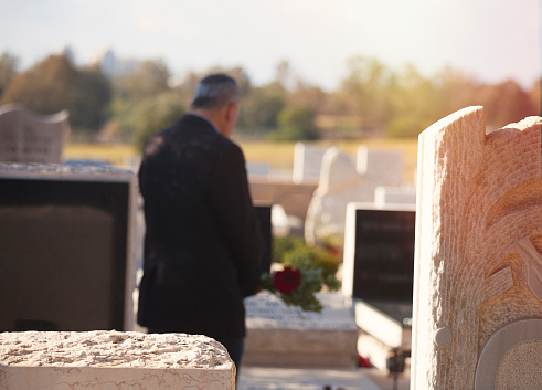 Man holding flowers and standing next to a tombstone, grieving, at the cemetery