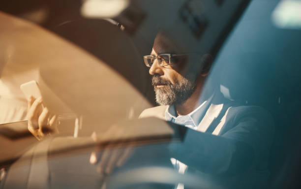 Executive drive. Closeup of late 40's handsome executive man driving in the back seat of a luxury limousine and using a smart phone.  Orange toned image. black taxi stock pictures, royalty-free photos & images