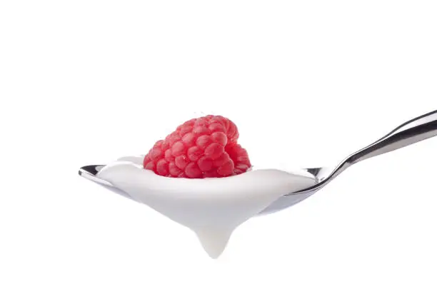 a spoon filled with yogurt with a whole fresh raspberry over it on a white background