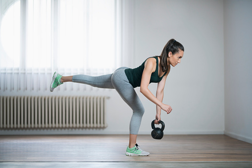 Beautiful, young female athlete exercising with a kettlebell.