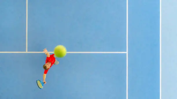 Tennis player in a red dress tries to hit a smash ball over the net. Dronen photo in a tennis hall.