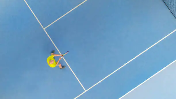 A Tennisplayer in a yellow dress shot from above with a drone. Waiting for a service on a blue floor