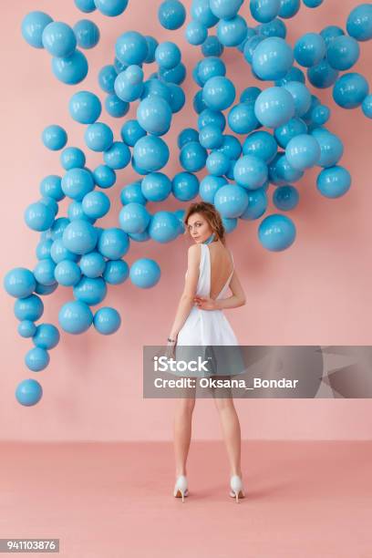 Young Woman In White Cocktail Dress Standing Back To Camera On Pink Wall Background With Blue Bubbles Hanging Dreaming Concept Stock Photo - Download Image Now