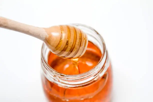 Close up of an organic sweet honey jar and a honey spoon on a white background from the above