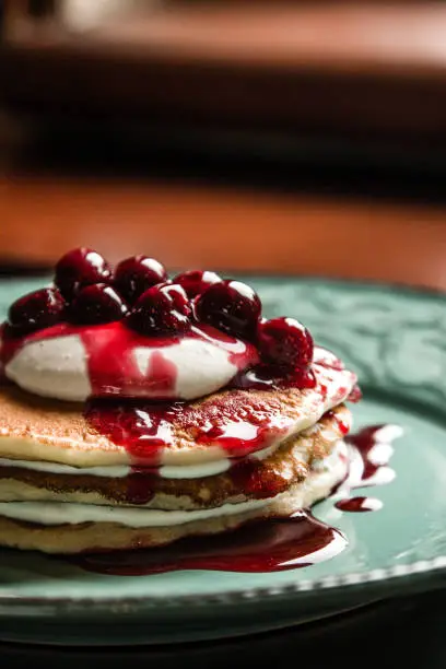American pancakes with fruit syrup and cherries on a pastel green rustic plate near the window on beautiful natural light