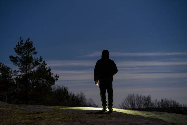 istock Human standing outdoor at night with flashlight and hoodie on head 941121864
