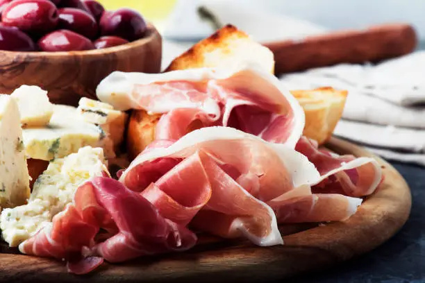 Snacks or antipasti, crostini, prosciutto, blue cheese and olives, gray background, selective focus