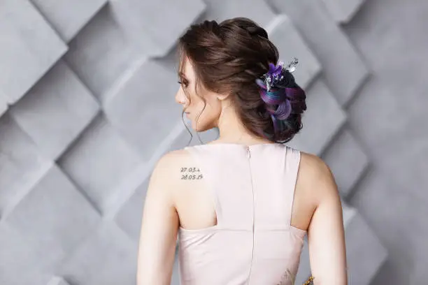Brunette woman hairdo french twist, rear view on gray fashion studio background. Shoulder wit numeric tattoo.