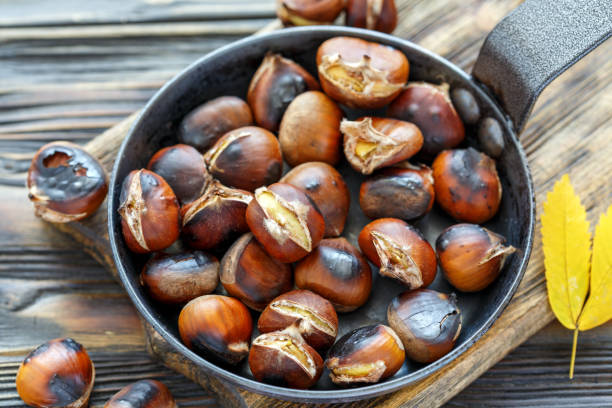 Roast chestnuts in a pan closeup. Cast iron skillet roasted chestnuts on the old wooden table, selective focus. chestnut food stock pictures, royalty-free photos & images