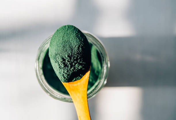 Spirulina powder in a wooden spoon Spirulina powder in a wooden spoon spirulina bacterium stock pictures, royalty-free photos & images