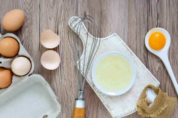 istock Fresh farm eggs on a wooden rustic background. Separated egg white and yolks, broken egg shells. Whipping eggs with whisk. Preparation of food from chicken eggs. The top view. View from above. 941159912