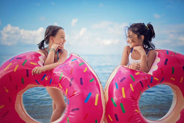 zwei mädchen am strand mit ihre donuts stehen und schauen einander - sea swimming greece women stock-fotos und bilder