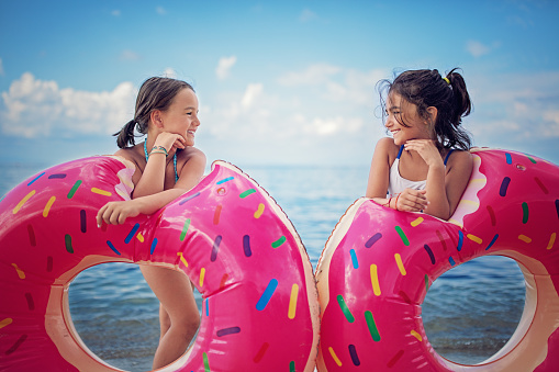 Two girls are standing on the beach with their donuts and looking each other