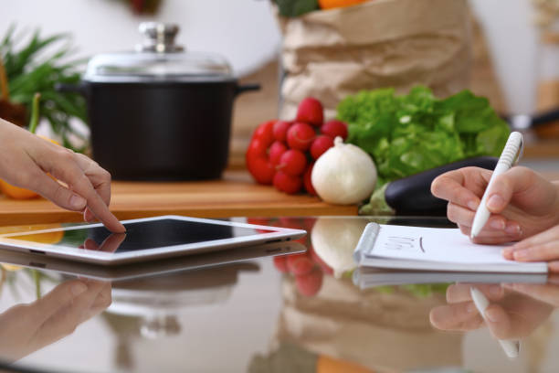 istock Closeup of human hands cooking in kitchen. Women discuss a menu using tablet computer. Copy space area at touch pad. Healthy meal, vegetarian food and lifestyle concepts 941171248