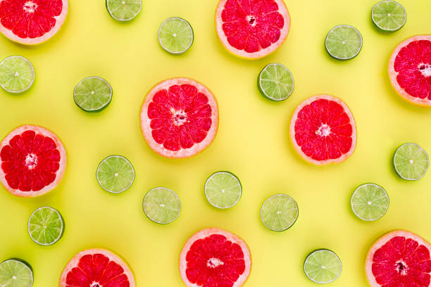 istock Background of red grapefruits and green limes split in half on yellow background 941183582