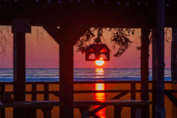 Photo of silhouettes of the pavilion and bird feeders against the backdrop of the sun setting in the winter lake