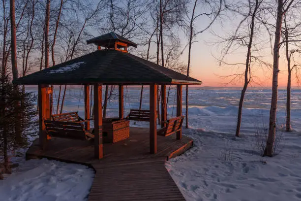 Photo of silhouettes of the pavilion and bird feeders against the backdrop of the sun setting in the winter lake