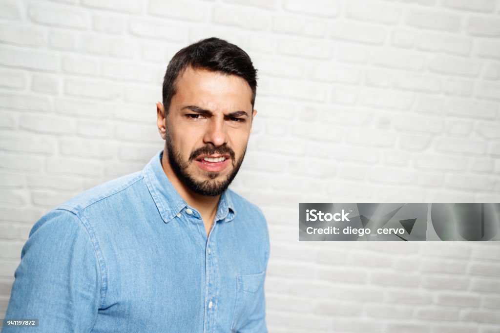 Facial Expressions Of Young Beard Man On Brick Wall Portrait of disgusted man, hispanic guy showing disgust for bad smell or taste. Copy space Men Stock Photo
