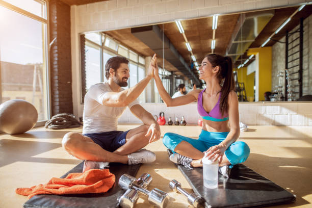 nahaufnahme von attraktiven hübschen jungen fitness paar händeklatschen zusammen beim sitzen auf den schwarzen matten und eine pause in der turnhalle vor dem spiegel. - coach individuality organized group gym stock-fotos und bilder