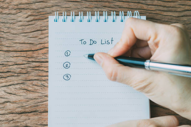 istock Hand holding black pen writing To Do List tasks prioritized by number on white paper notepad on wood table 941206498