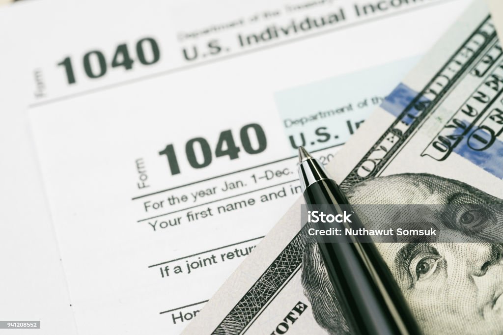 Tax time concept, pen on US dollar bills with 1040 US individual income tax filling form, calculate from yearly revenue to pay the goverment Tax time concept, pen on US dollar bills with 1040 US individual income tax filling form, calculate from yearly revenue to pay the government. Annual Event Stock Photo
