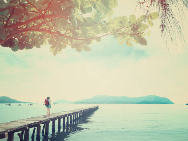 Asian woman backpacker tourist standing on old wooden bridge at pier in the sea, vintage filter effect.