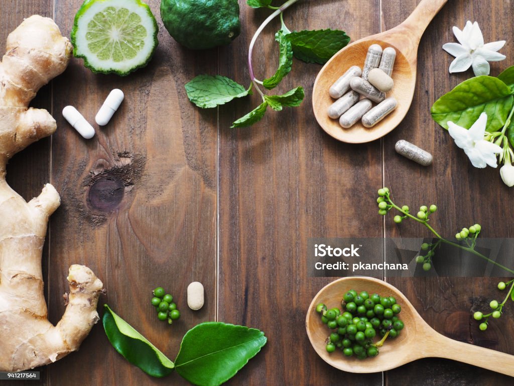 herbal pills in wooden spoon herbal pills in wooden spoon with ginger root, Kaffir lime fruit and flower on dark brown wood background with copy space. Above view. Herbal Medicine Stock Photo
