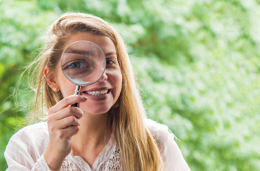 Great concept of research and investigation, young blond woman looking through the magnifying glass.