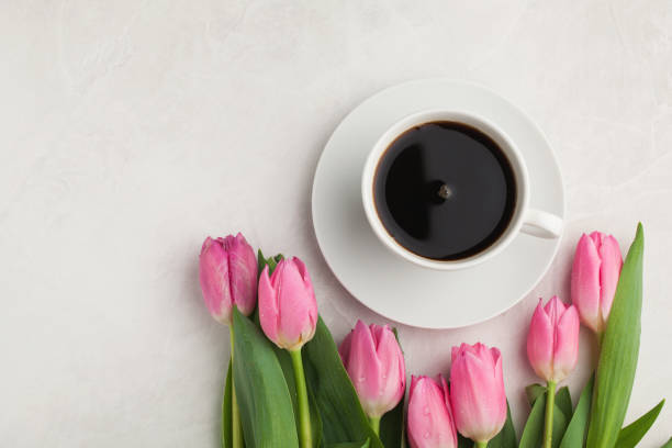 istock Black coffee in white Cup with pink tulips on light stone background. Top view with copy space 941225844