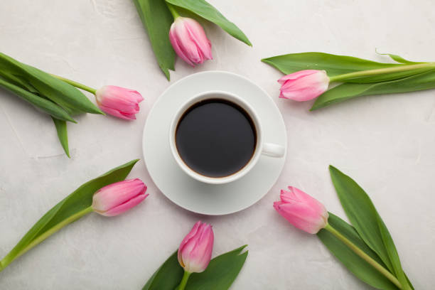istock Black coffee in white Cup with pink tulips on light stone background. Top view 941225846