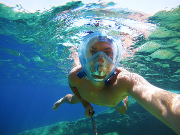 istock Young joyful handsome man taking a photo with a selfie stick while diving under the sea surface. 941228028