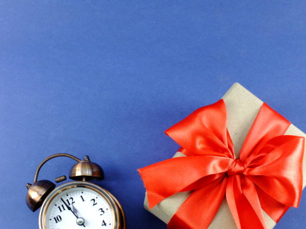 istock alarm clock and gift box wrapped in recycled paper with ribbon bow isolated on blue background 941237314