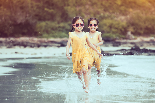 Two cute asian little child girls having fun to play and run on beach together in summer vacation in vintage color tone